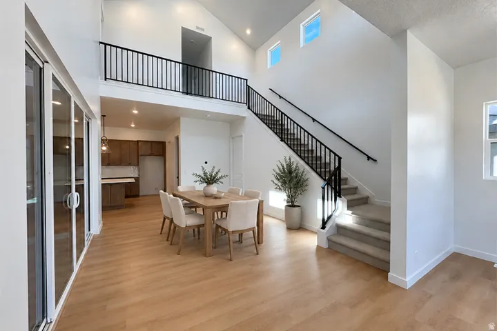 Vaulted ceiling, wood-finish flooring, glass sliding doors, open-riser staircase with metal railing, and upper-level windows