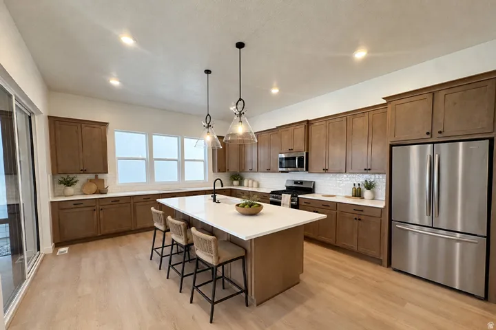 Gourmet kitchen featuring wood-finish cabinetry, stainless steel appliances, a center island with seating, a tile backsplash, and multiple windows