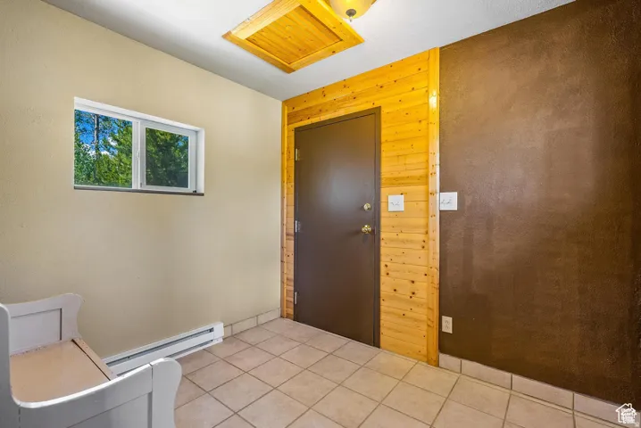 Entryway featuring tile flooring, a dark brown door framed by vertical wood paneling, a recessed wall heater, and a horizontal window