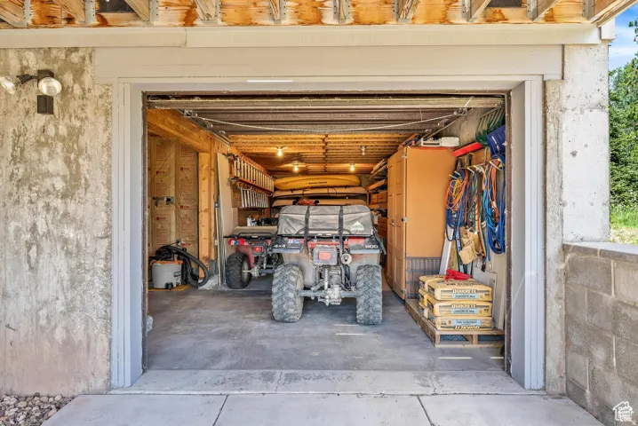 Spacious garage with exposed wood framing, concrete flooring, built-in shelving, and overhead lighting
