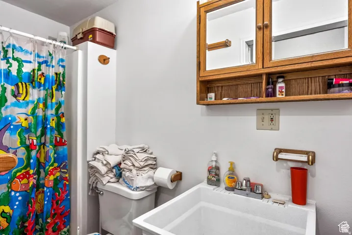 Bathroom featuring a utility sink, toilet, and shower with a white surround