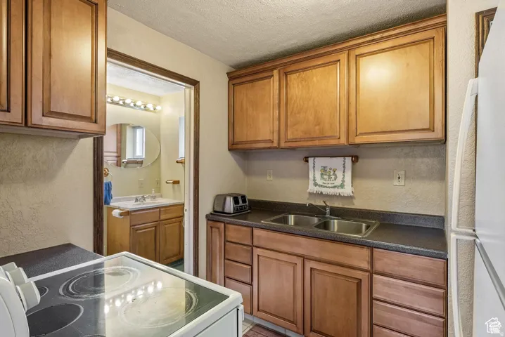 Compact kitchen featuring wood-finish cabinetry, a dual basin stainless steel sink, and dark countertops
