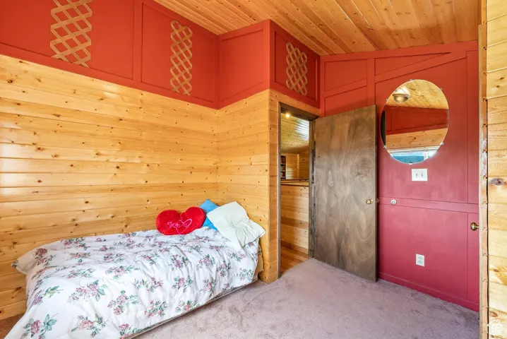 Room featuring wood-plank walls and ceiling, carpeted flooring, and a red accent wall with decorative lattice panels