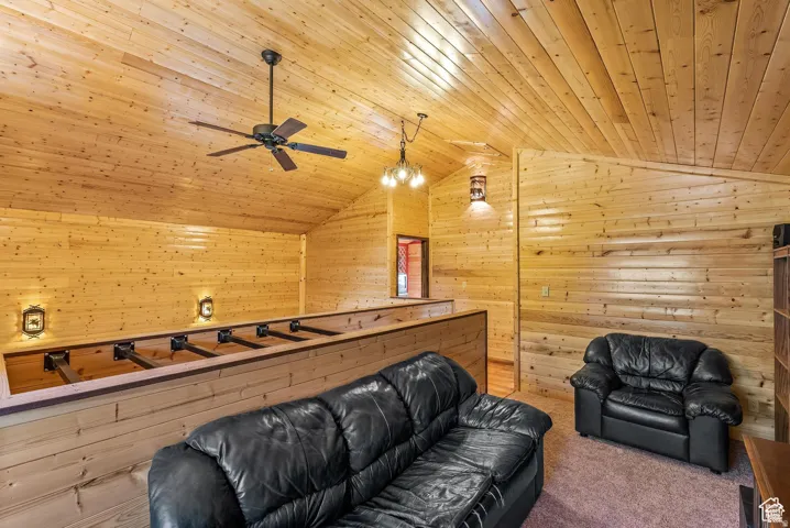 Vaulted ceiling loft space featuring extensive wood paneling, a ceiling fan, and decorative wall sconces