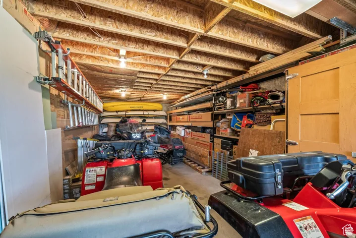 Expansive garage space featuring exposed wood joist ceilings, multiple overhead light fixtures, extensive built-in shelving, and a wood-paneled utility door
