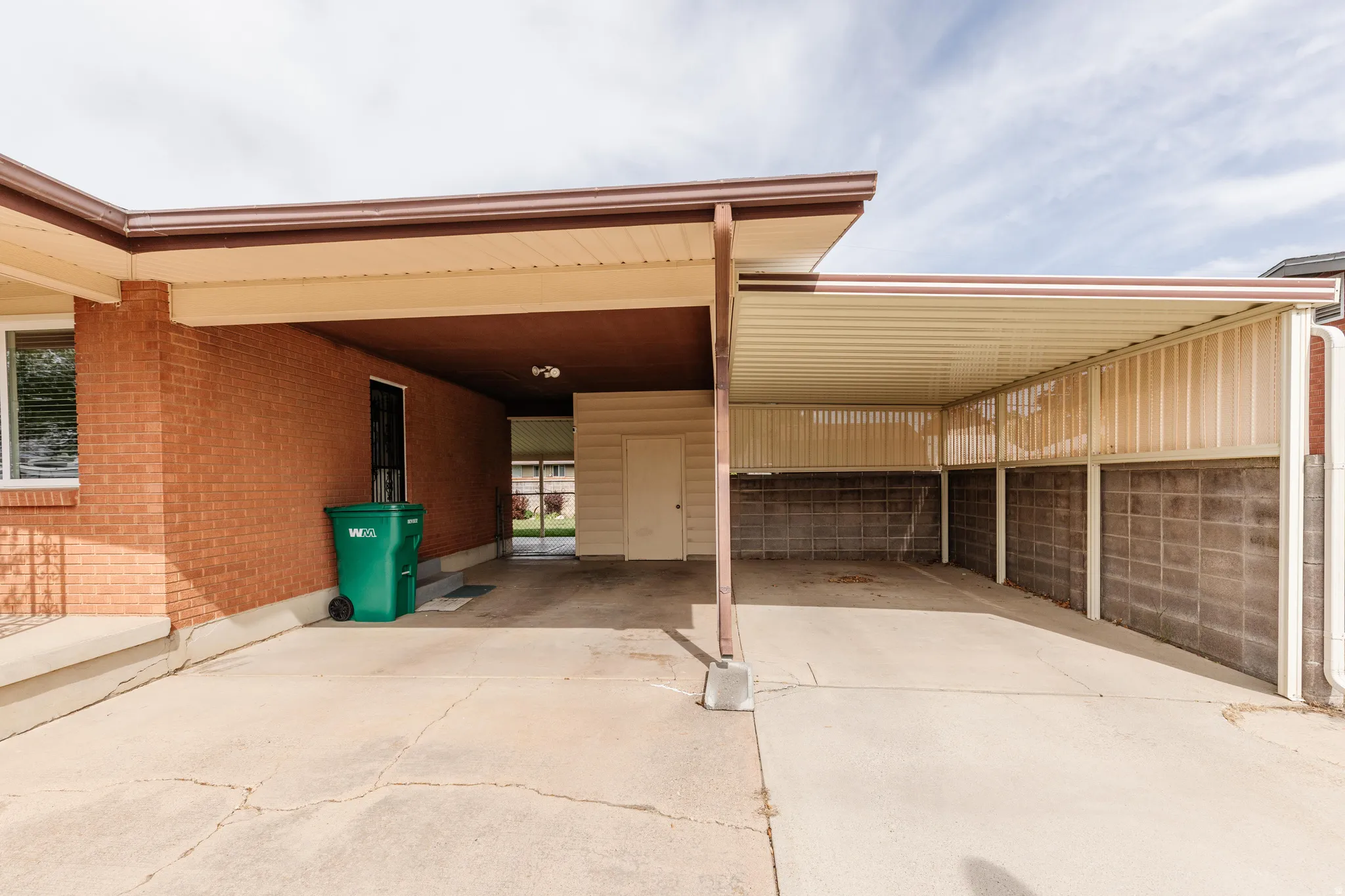 Expansive covered carport featuring a concrete slab, brick exterior wall, and additional covered patio area