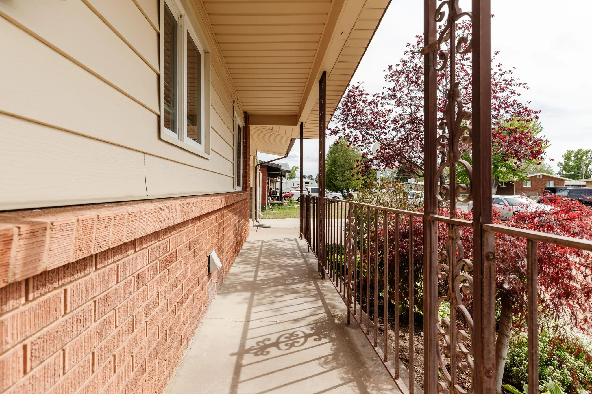 Covered porch entry featuring decorative metal railings, a brick foundation, and horizontal siding