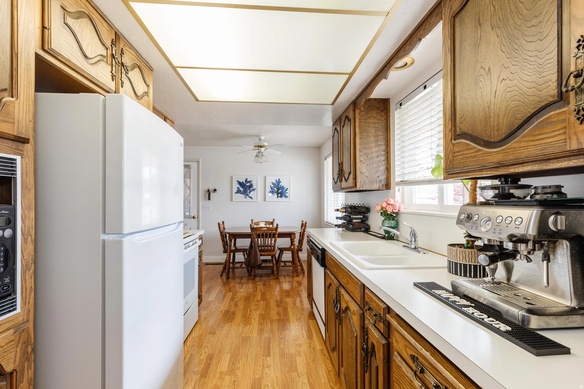 Galley kitchen featuring wood-finish cabinetry, white countertops, a double basin sink, and wood-finish flooring
