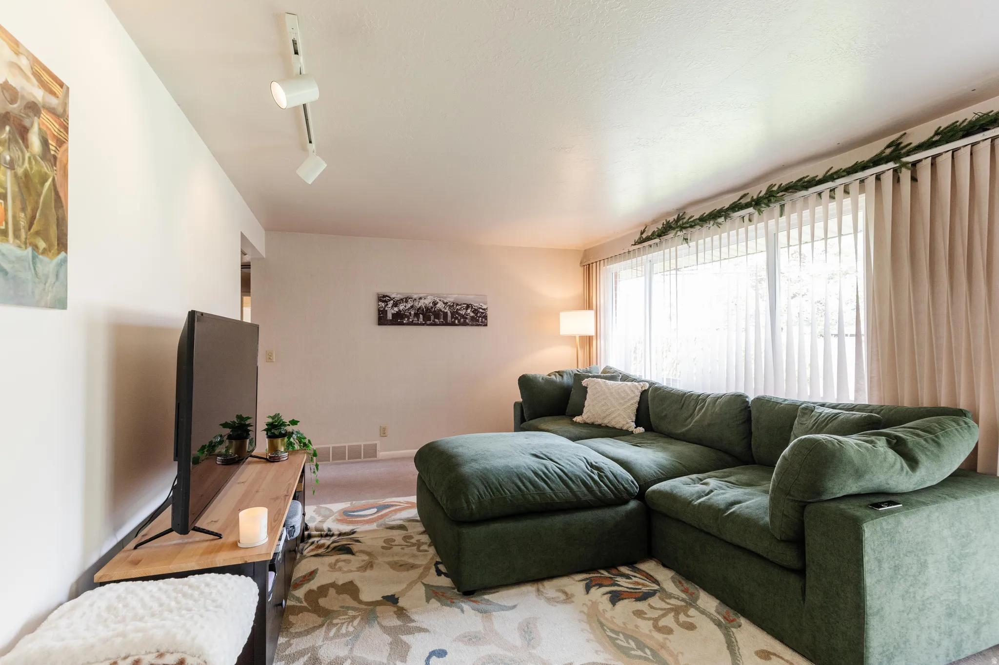 Living room featuring white walls, track lighting, and a large window with vertical blinds and drapes