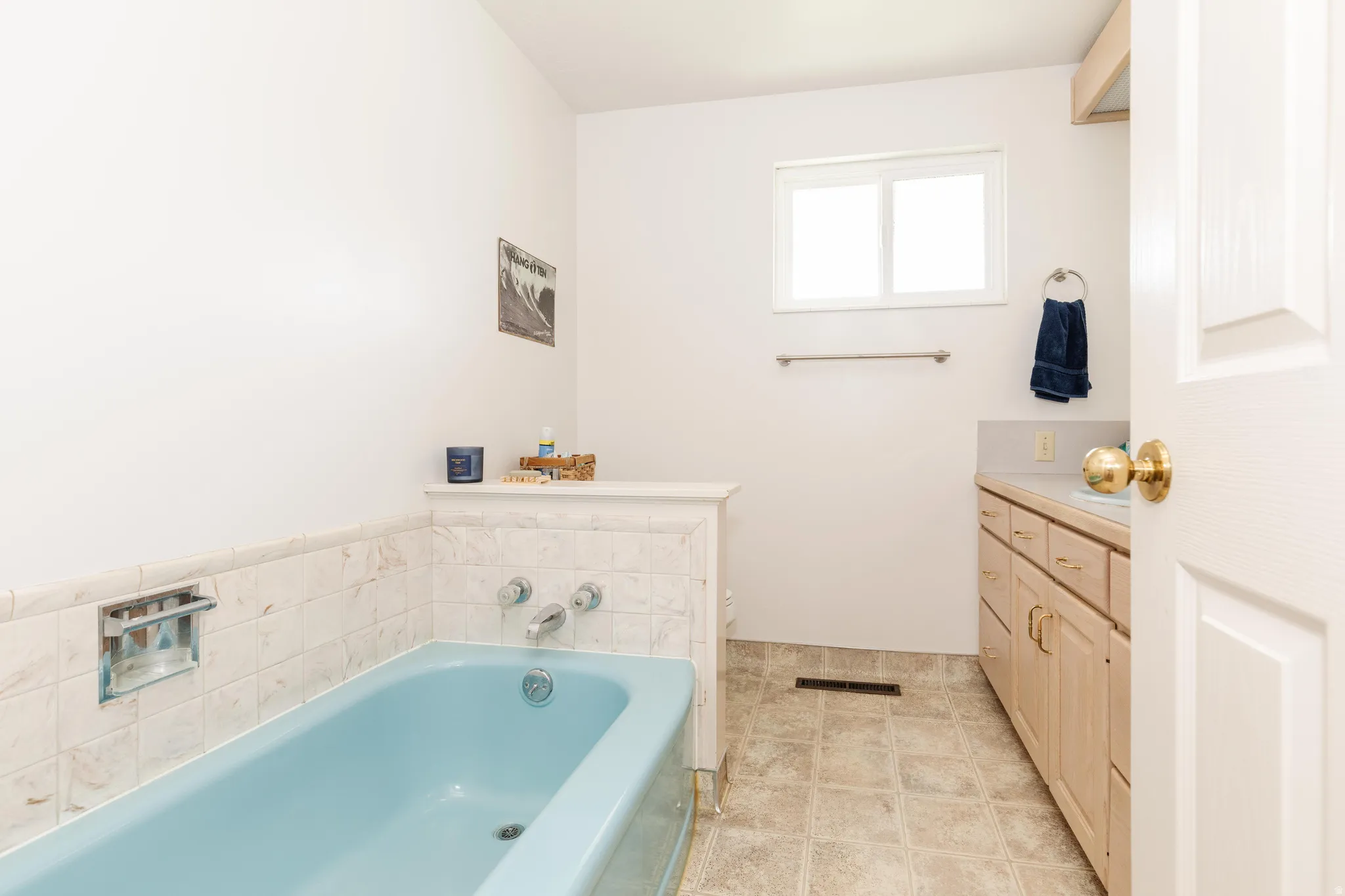 Bathroom featuring a built-in tub with tile surround, a single window, a vanity with wood-finish cabinetry, and tiled flooring