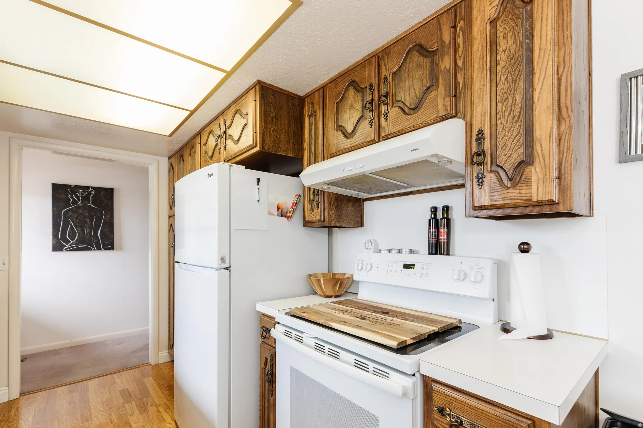 Kitchen featuring wood cabinetry with decorative hardware, white appliances, and a white countertop