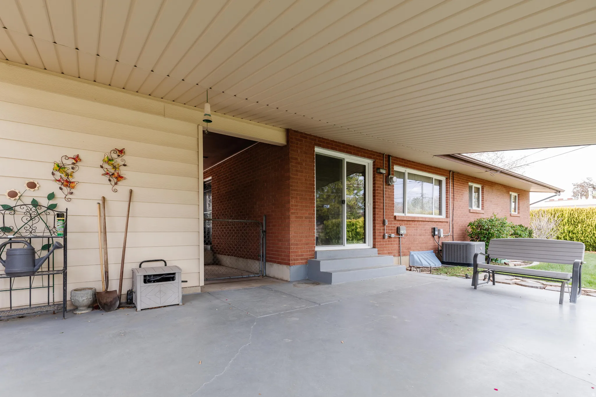 Covered patio area featuring a concrete surface, brick exterior wall, sliding glass door, and a built-in bench