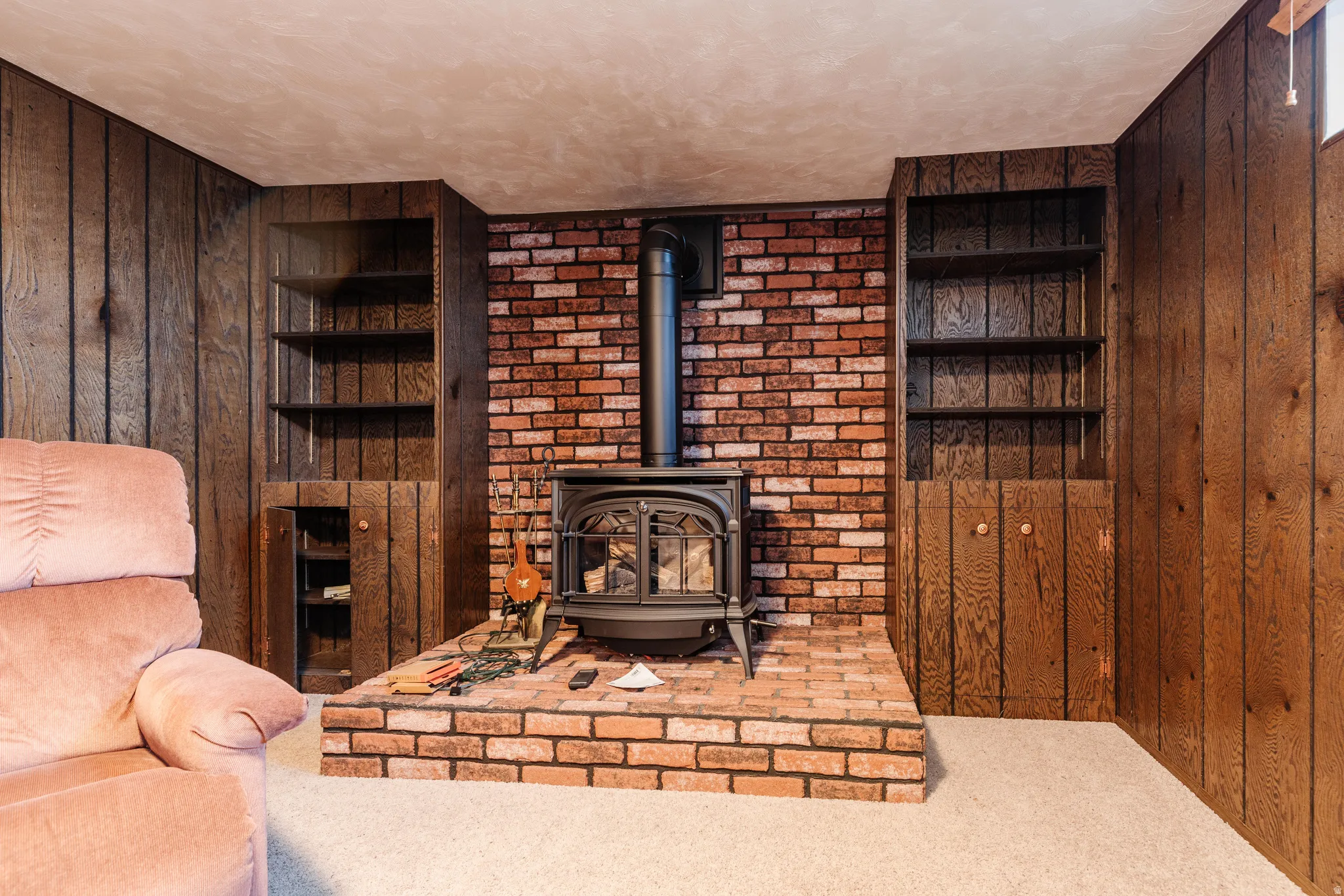 Wood-paneled wall surfaces frame a central brick feature wall with a wood-burning stove on a raised brick hearth