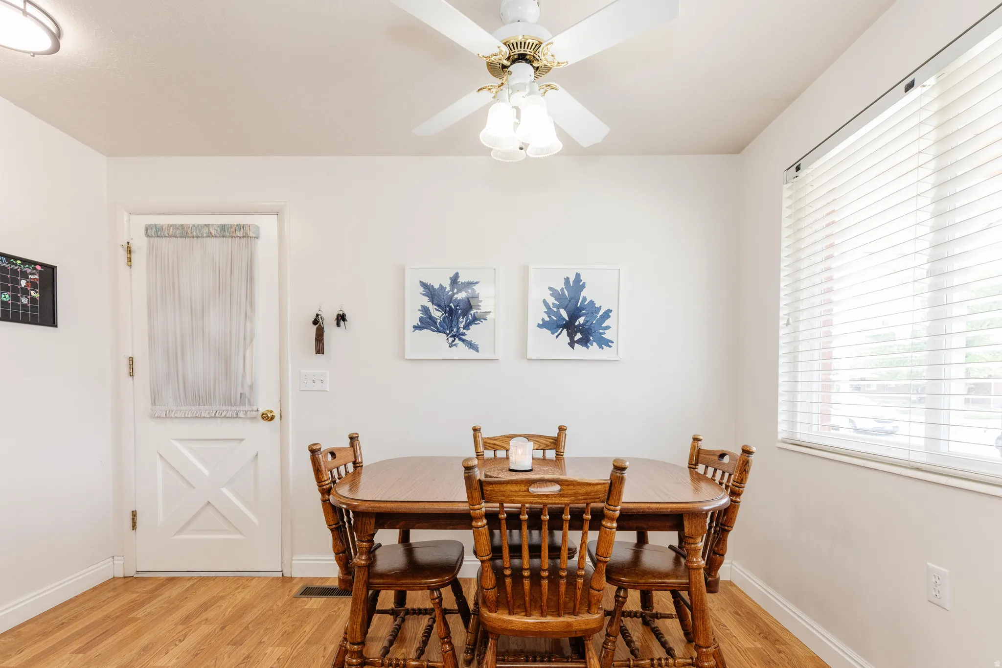Dining area featuring wood-finish flooring, a ceiling fan with integrated lighting, a window with blinds, and a white paneled door