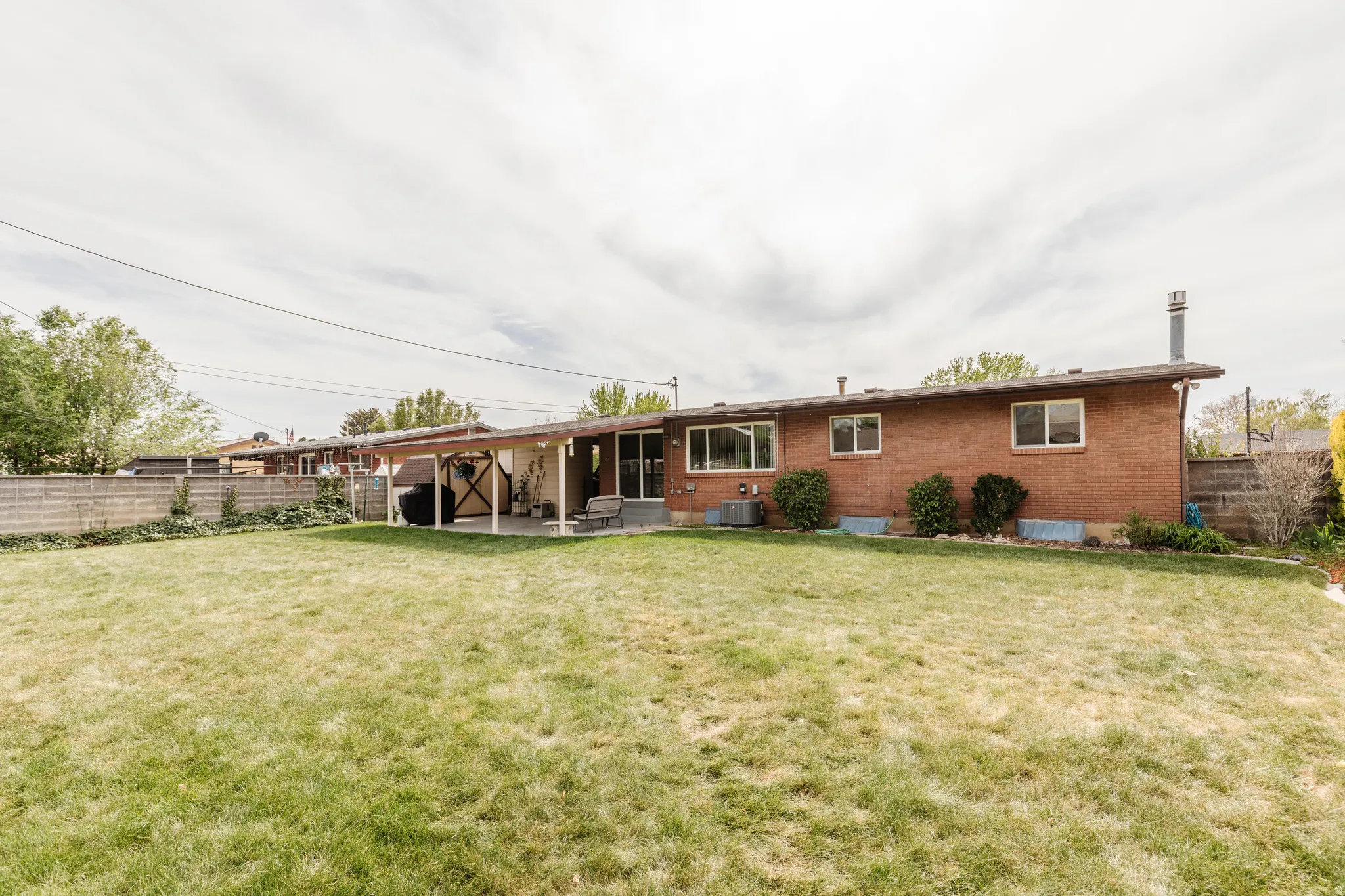 Expansive backyard featuring a manicured lawn, a full-brick exterior, multiple windows, a covered patio, and mature perimeter fencing