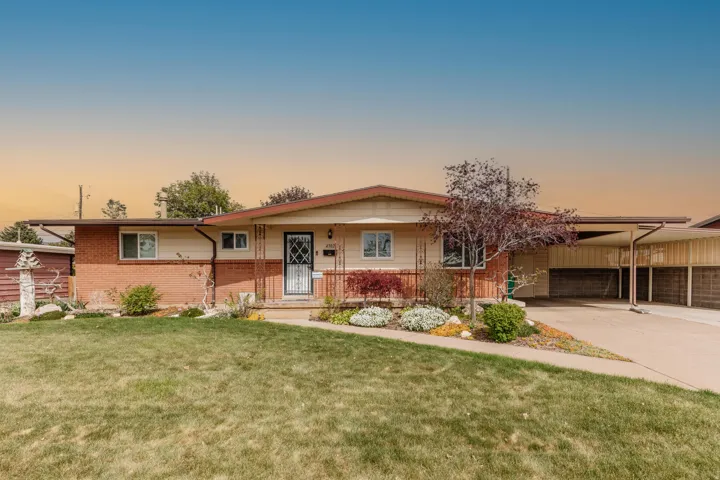 Ranch-style residence featuring a brick and siding exterior, an attached carport, a covered front porch with wrought iron railing, and a mature front yard with landscaping