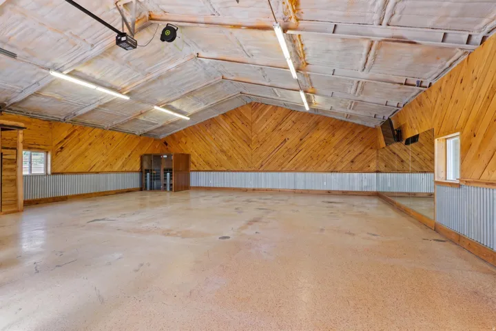 Spacious interior featuring a high vaulted ceiling with exposed insulation, wood-paneled walls, corrugated metal wainscoting, and a polished concrete floor