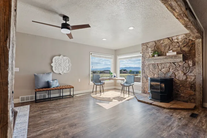 Living area featuring wood-finish flooring, a stone accent wall with a built-in wood mantel, and large windows