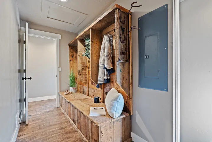 Built-in wooden bench with open storage cubbies and coat hooks, set against a neutral wall color