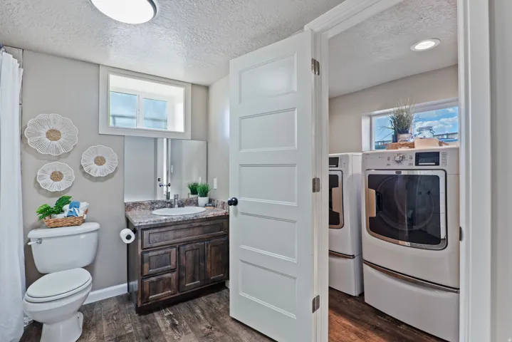 Full bathroom featuring a wood-finish vanity with a stone-look countertop, a white toilet, and wood-finish flooring