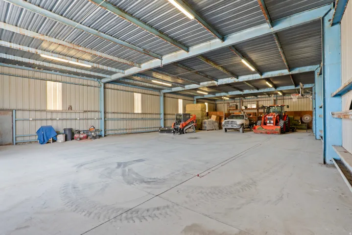 Spacious metal building featuring a concrete floor, corrugated metal ceiling, exposed structural beams, and multiple fluorescent light fixtures