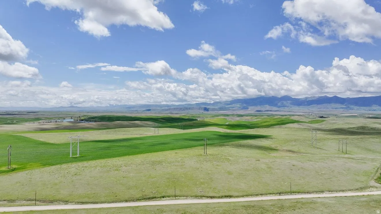 Expansive open land featuring rolling green hills and distant mountains under a blue sky with scattered clouds