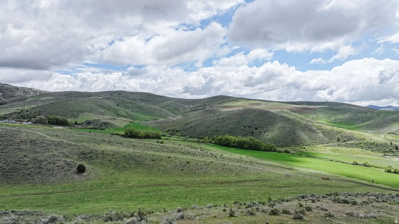 Rolling green hills and distant mountain ranges with varying vegetation patterns under a sky with scattered clouds
