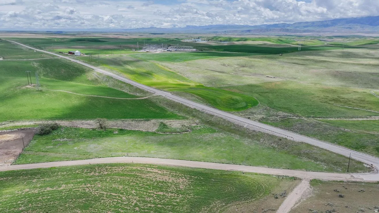 Expansive agricultural landscape featuring a paved road traversing verdant fields under a partly cloudy sky