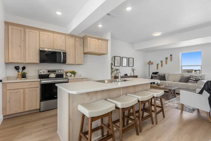 Open-concept kitchen featuring light wood-finish cabinetry, stainless steel appliances, and a central island with integrated sink