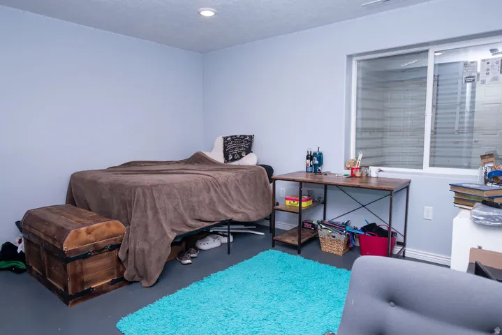 Recessed lighting illuminates a room featuring a large egress window, light-toned walls, and grey flooring