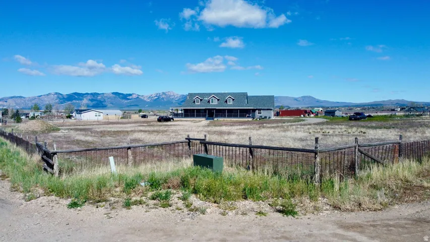 Expansive property featuring a single-family home with multiple dormer windows, a covered front porch, and a gravel driveway