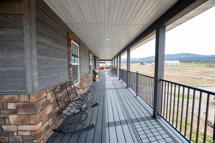 Expansive covered porch featuring composite decking, a black metal railing, and stone siding accents