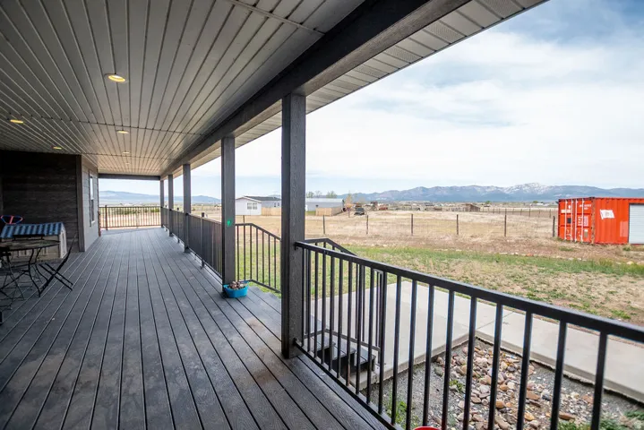 Spacious covered porch with composite decking, recessed lighting, substantial support pillars, and black metal railings