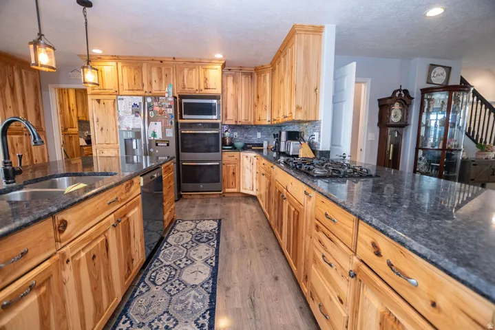 Kitchen featuring natural wood cabinetry, dark stone-finish countertops, stainless steel appliances, wood-finish flooring, and recessed lighting