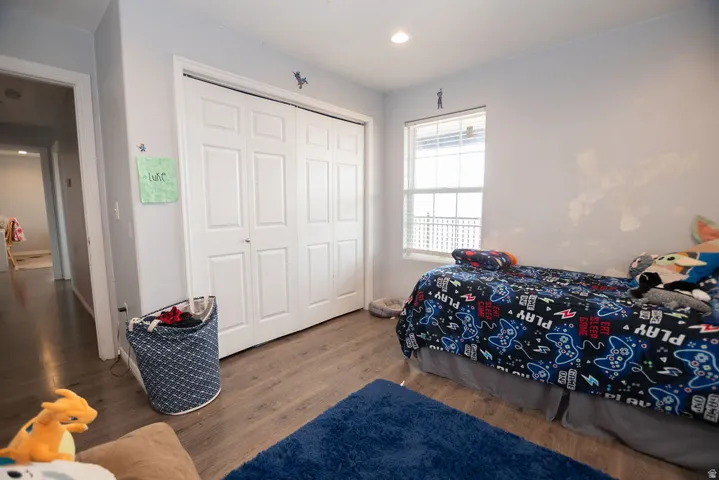 Room featuring light gray walls, wood-finish flooring, a white bi-fold closet door, a window with horizontal blinds, and a recessed ceiling light