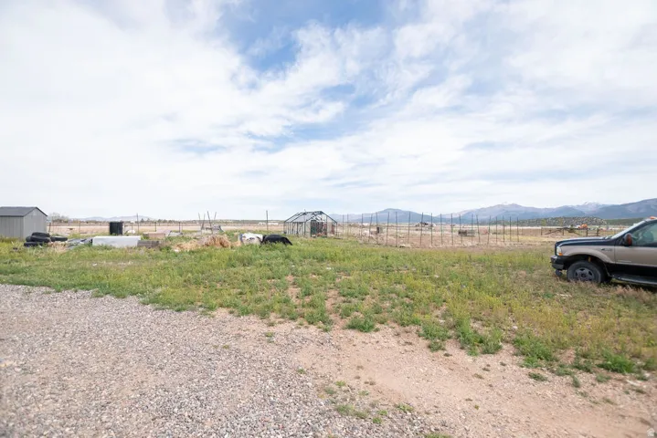 Expansive gravel driveway leading to a large, undeveloped lot with a storage shed and a greenhouse structure