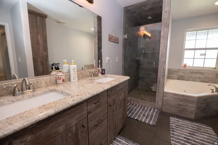 Dual vanity with light-toned countertop and wood-finish cabinetry, frameless glass shower enclosure, and a built-in corner soaking tub with tiled surround