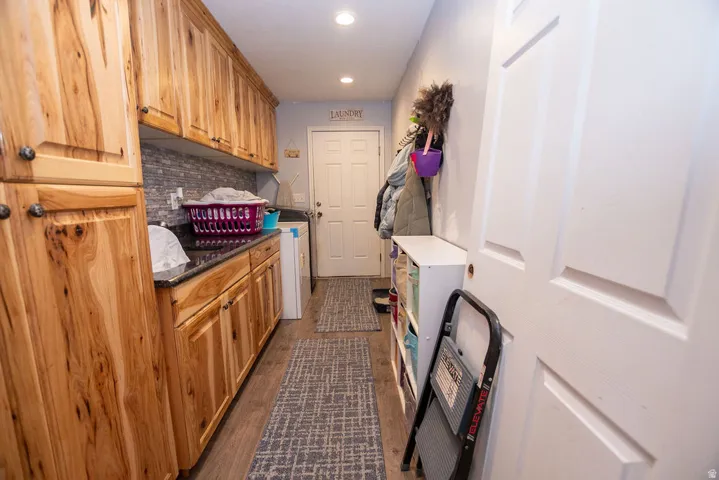 Laundry room featuring extensive wood cabinetry, dark countertops, tile backsplash, and recessed lighting