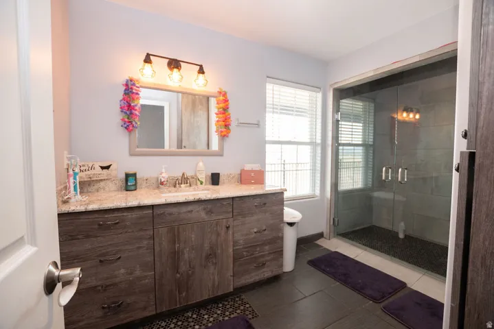 Bathroom featuring a double vanity with stone-finish countertop, wood-finish cabinetry, a framed mirror, and a three-bulb vanity light fixture