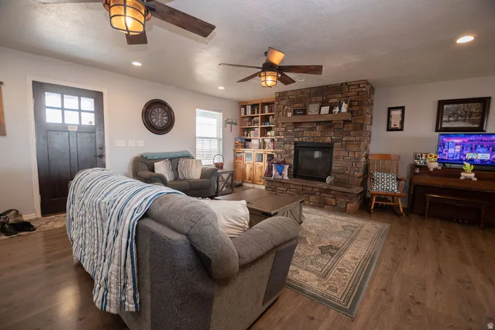Spacious living area featuring stone-clad fireplace, wood-finish flooring, and ceiling fans with integrated lighting