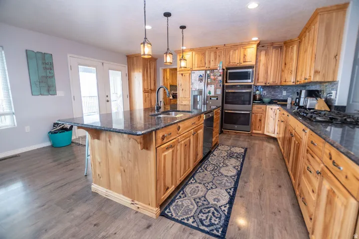 Kitchen featuring a central island with a sink, granite countertops, wood-finish cabinetry, stainless steel appliances, and wood-finish flooring