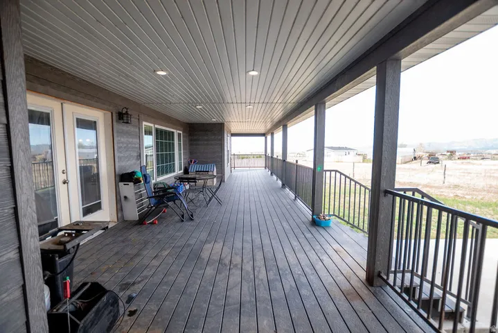 Expansive covered porch featuring wood-finish decking, integrated recessed lighting, and black metal railings with integrated stairs