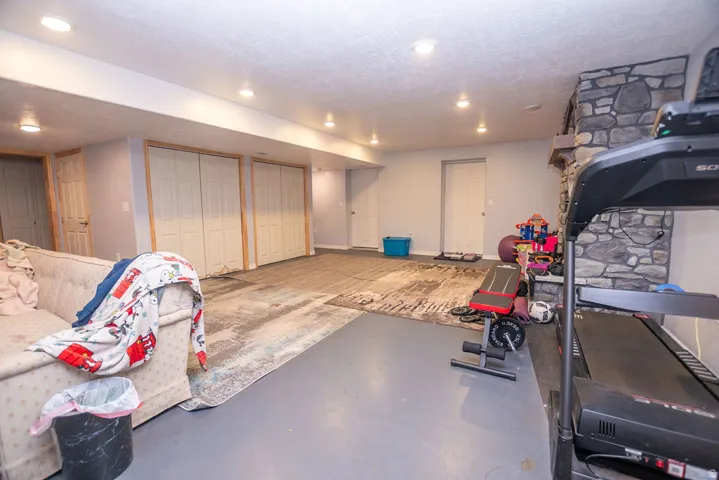 Spacious lower level featuring a stone fireplace, recessed lighting, painted concrete flooring, and multiple bi-fold closet doors with natural wood trim