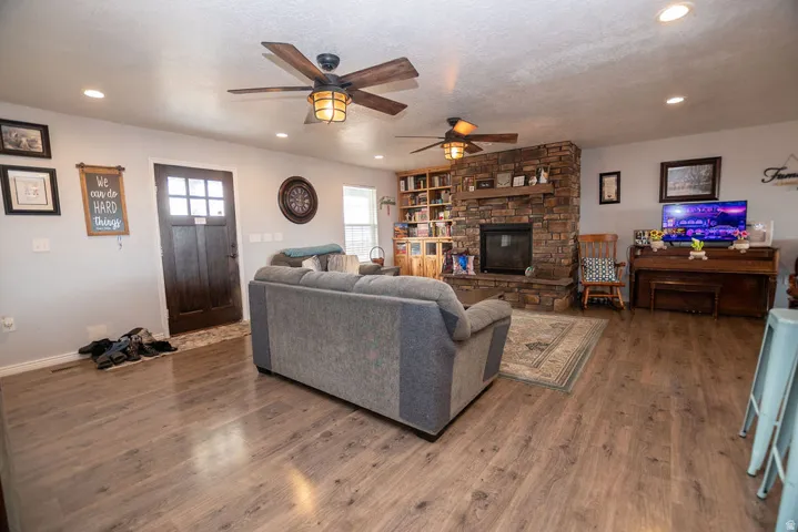 Spacious living area featuring wood-finish flooring, a stone fireplace with a built-in mantel, recessed lighting, and two ceiling fans