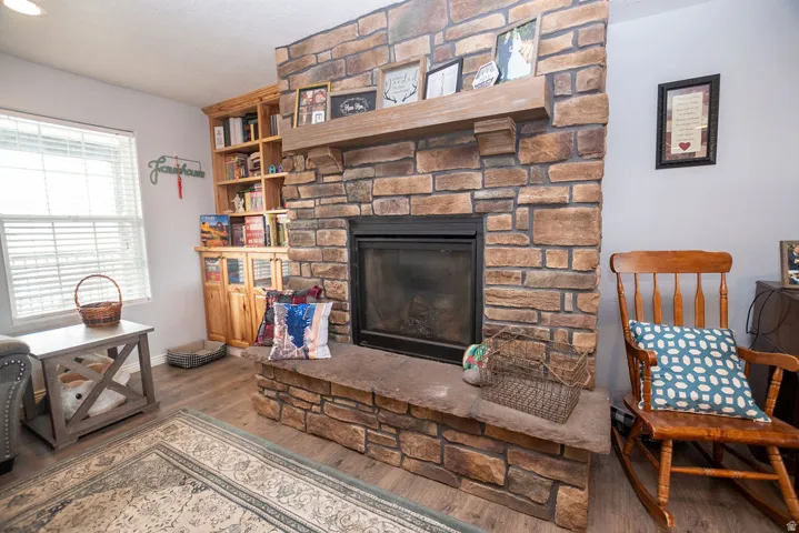 Stacked stone fireplace with a substantial wood mantel, integrated firebox, stone hearth, and wood-finish flooring