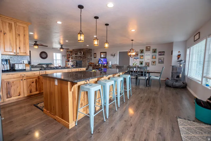 Open-concept kitchen and dining area featuring natural wood cabinetry, a large kitchen island with counter seating, dark stone countertops, wood-finish flooring, and recessed lighting