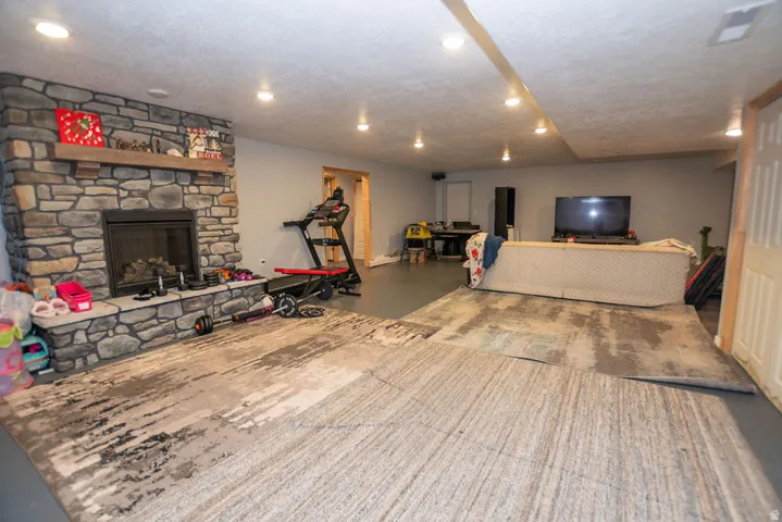 Spacious lower-level area featuring a stone-clad fireplace with a wood mantle, recessed lighting, and light grey walls