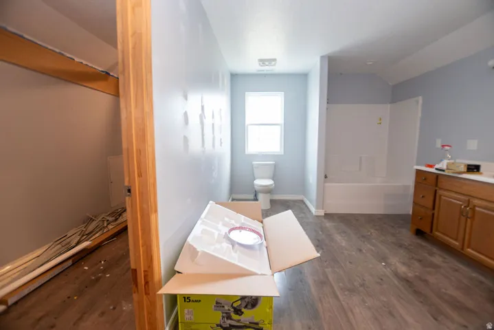 Bathroom featuring a wood-finish flooring, a window, a white toilet, and a white tub with shower surround