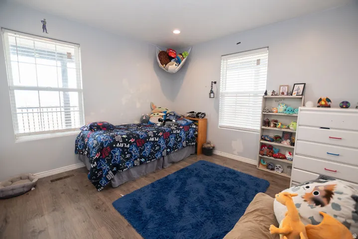 Spacious room featuring two windows with horizontal blinds, wood-finish flooring, and light gray walls