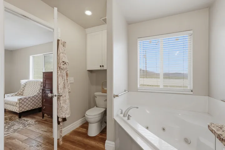 Built-in jetted tub with chrome fixtures, a window with horizontal blinds, and a built-in wall cabinet above the commode